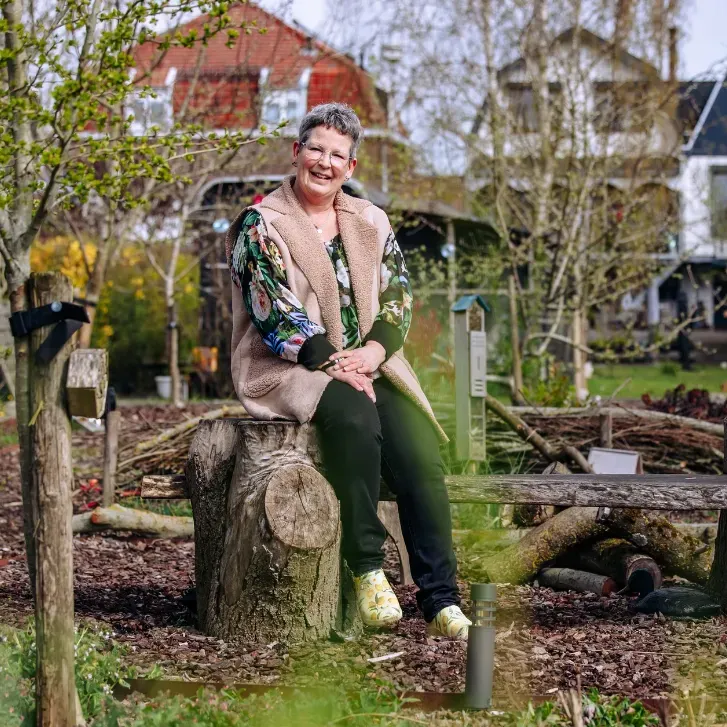 Astrid zit op een boomstronk in haar groene tuin met natuurlijke elementen en nestkastjes voor dieren.